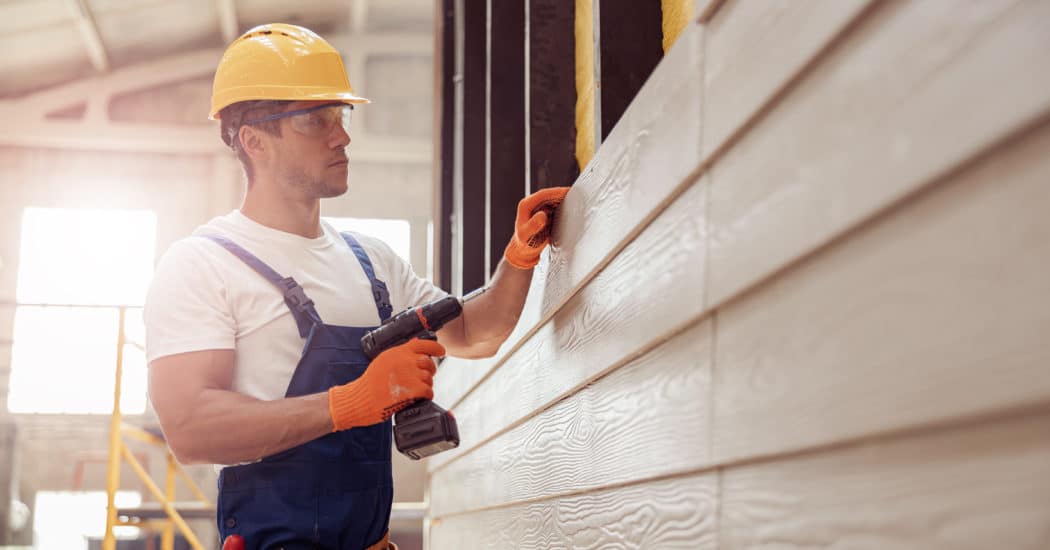 Handsome young man builder installing exterior wood siding
