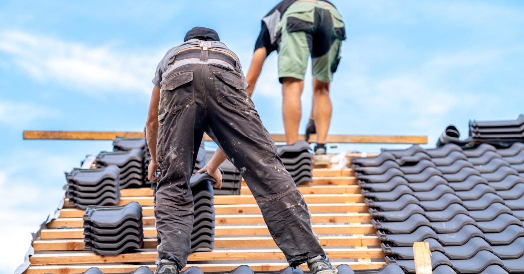 workers build a new roof from ceramic tiles on wooden beams
